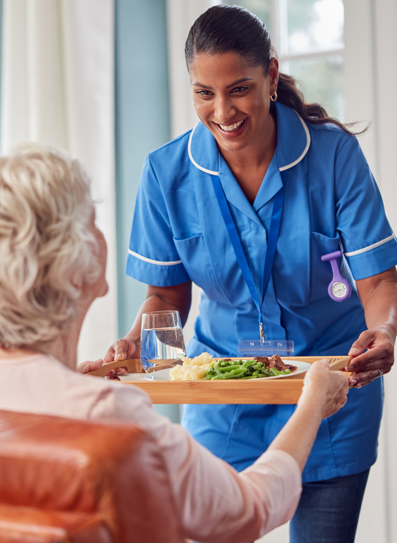 Altenpflegerin bringt Seniorin ihr Mittagessen im Altersheim